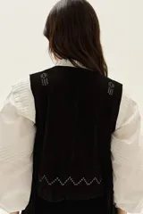 Chaleco de cuero negro con flecos largos en los laterales y detalles bordados en hilo blanco en la espalda.