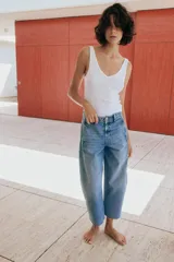 Jeans de tiro medio con pernera holgada tipo barrel que se estrecha hacia el tobillo, acabado con bajo sin costura, bolsillos delanteros y bolsillos de plastrón en la espalda. Cierre frontal con cremallera y botón.