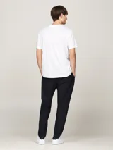 Remera blanca de algodón con cuello redondo y manga corta. Presenta una banda horizontal con los colores distintivos de Tommy Hilfiger y el logo bordado en el pecho.