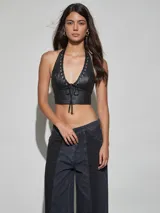 Top halter de cuero sintético negro con escote en V profundo, detalles de ojales metálicos y cordón ajustable frontal.