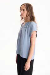Blusa negra de manga corta, confeccionada en tela crepé, con detalle de fruncido en el escote redondo y pequeña abertura frontal en V.