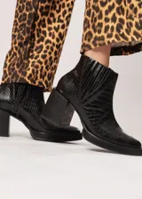 Botín negro de cuero con elástico lateral y cierre interno. Tiene plataforma delantera de 2 cm y taco de 8 cm.