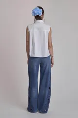 Camisa azul marino sin mangas con cuello clásico, abotonada al frente y detalle de plisados verticales en el pecho.