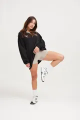 Camiseta negra oversize de manga larga con cuello en V blanco y logo en el pecho.