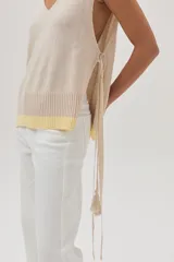 Chaleco tejido de algodón color beige, con escote en V, lazos laterales y terminaciones con pompones.