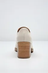 Zapato de cuero color beige, con taco de madera y suela dentada. Presenta un diseño slip-on con detalles de textura en relieve en los laterales y el empeine.