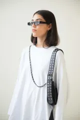 Cartera tipo baguette negra de cuero vacuno con textura tipo piel de cocodrilo. Tiene correa de cuero ajustable con detalles de tachas y cadena metálica plateada. El frente presenta un aplique de cuero con hebilla metálica plateada con tachas.