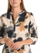 Blusa de gasa con estampado floral en tonos blanco y negro, cuello a la base con escote en V y cierre frontal parcial con botones. Presenta mangas tres cuartos con puños rectos.