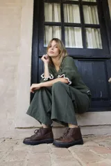 Borcegos de cuero charolado negro con cordones jaspeados en tonos marrones y suela track dentada con costura blanca visible.