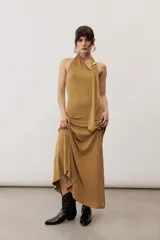 Vestido largo negro de corte al cuerpo con cuello halter y detalle de hebilla metálica dorada en el hombro con tira drapeada.