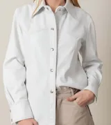 Camisa de cuero ovino italiano color blanco, de corte holgado, con cuello clásico, cierre frontal con broches metálicos, bolsillos laterales y puños con broches.