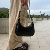 Cartera de hombro tipo hobo en eco cuero color negro con textura efecto cocodrilo, diseño compacto y cierre superior con herrajes dorados.