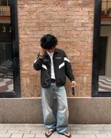 Campera deportiva negra con cuello alto, cierre frontal completo y diseño oversize. Cuenta con bandas blancas diagonales en las mangas y el torso, y texto estampado en el pecho.