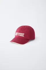 Gorra de béisbol azul marino con visera curva y detalle de borde en color crema. Presenta un bordado frontal con la palabra 'LONDON' en tipografía estilo varsity y texto adicional debajo.
