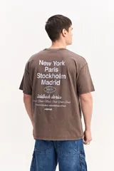 Remera oversize de algodón color marrón con efecto acid wash y diseño tipográfico en la espalda que incluye nombres de ciudades.