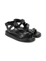 Sandalia de cuero rústico color negro, con suela robusta de PVC, múltiples tiras cruzadas, sujeción para el dedo y tira ajustable con hebilla en el tobillo.