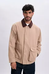 Campera color taupe de corte recto, con cuello camisero de pana marrón oscuro, cierre frontal oculto con botones a presión y grandes bolsillos frontales con solapa.
