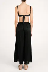 Pantalón fluido de corte ancho, color negro con sutil acabado brillante, cintura elástica y diseño holgado.