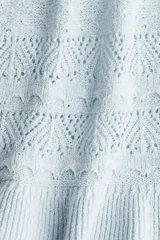 Musculosa corta celeste en tejido de punto calado estilo crochet, con escote redondo pronunciado con ribete festoneado y bajo acanalado de volado. Sin mangas.