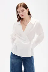Camisa blanca de algodón con diseño cruzado y anudado lateral, cuello camisero y mangas largas con puños.