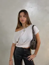 Remera de corte holgado con diseño de un hombro descubierto, confeccionada en tela suave con estampado de pequeños lunares. Presenta un ajuste elástico en la cintura que le otorga una caída drapeada.