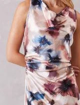 Vestido midi de satén fluido con estampado floral en tonos beige, azul y borravino. Presenta cuello volcado, diseño sin mangas y un drapeado lateral fruncido en la cintura que aporta movimiento a la falda de corte evasé.