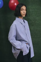 Camisa de corte oversize con estampado a rayas verticales en tonos azul y blanco, cuello clásico y cierre frontal con botones.