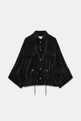 Cazadora satinada de color negro, con cuello subido, bolsillos con solapa en el pecho y cordón ajustable en la cintura. Cierre frontal con botones metálicos y mangas anchas.