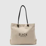 Bolso tipo tote de lino en color beige, con diseño de manijas largas de cuero sintético negro y estampa frontal con texto en negro.