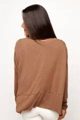 Remera de manga larga color marrón, confeccionada en una mezcla de viscosa, lino y elastano. Presenta un corte relajado con diseño asimétrico, destacando una costura horizontal en la parte frontal y bordes sin remate que le otorgan un estilo descontracturado.