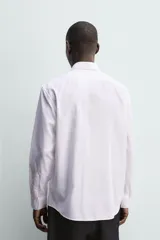 Camisa de corte regular fit con cuello italiano y manga larga con puños abotonados. Presenta un diseño de rayas verticales finas en tono suave sobre fondo claro, con cierre frontal de botones.