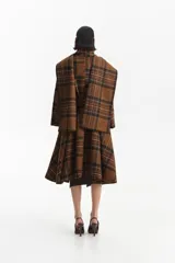 Abrigo largo tipo trench con estampado a cuadros en tonos marrones. Presenta un cuello que simula una bufanda integrada, cierre mediante lazo ajustable en la cintura y mangas largas. Confeccionado en una mezcla de lana y poliéster con forro interior.