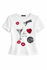 Remera blanca de algodón con estampado frontal que incluye una copa de martini, un corazón rojo, una bola de espejos y labios rojos, junto con la frase 'Amazon must haves'.