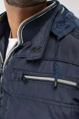 Campera de nylon color azul marino con cierre frontal completo, capucha desmontable y puños elásticos. Presenta bolsillos con cierre y logo aplicado en la manga.