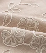 Camisa de poliéster color beige con bordado floral blanco, de corte regular, cuello inglés, manga corta y abotonada en el frente.