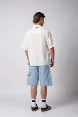 Camisa de hombre de manga corta color beige claro, confeccionada en lino. Tiene cuello clásico, cierre frontal con botones y corte recto.