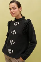 Sweater de lana color celeste, con cuello redondo, mangas largas y volados decorativos en los hombros. Presenta bordados florales artesanales en el frente y detalles de tejido calado vertical.