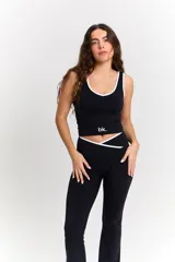 Conjunto deportivo compuesto por un top y un pantalón largo. El top es negro con ribetes blancos, escote redondo y logo 'bk.' estampado en el frente. El pantalón es negro, de corte acampanado, con cintura cruzada en V y detalle de ribete blanco.