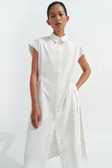 Vestido midi camisero de algodón color negro, con cuello solapa, sin mangas y cierre frontal con botones ocultos por solapa. Incluye cintura ajustable con tiras de lazada lateral en el mismo tejido.