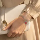 Pulsera de acero con cadena doble y dije redondo central que presenta una piedra roja tipo coral rodeada por un detalle trenzado.