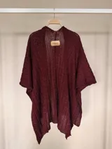 Ruana tejida de algodón con hilo lurex en punto jersey, color azul, con diseño amplio y detalle de etiqueta de cuerina en la parte posterior.