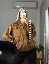 Campera tipo bomber confeccionada en gamuza, con cierre frontal metálico y detalle de flores bordadas en relieve en el frente.