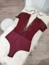Body de lycra color bordó con mangas cortas de encaje y detalle de encaje vertical en el frente. Presenta un diseño con espalda descubierta y tiras finas para atar en el cuello.