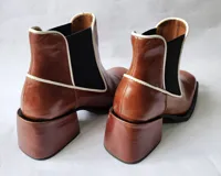 Bota tipo chelsea de cuero color óxido, con elástico lateral negro y ribetes en color crema. Presenta un taco cuadrado robusto y punta cuadrada.