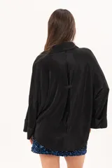Camisa negra plisada de manga larga con puños vueltos, cuello camisero y cierre frontal de botones claros.