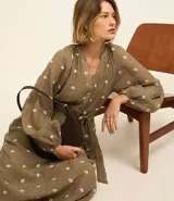 Vestido largo evasê color marrón con estampado de flores blancas, cuello en V, mangas largas abullonadas y cinturón de lazo.