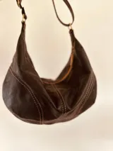 Cartera tipo banana bag de cuero color marrón oscuro, con correa ajustable para usar al hombro o cruzada.