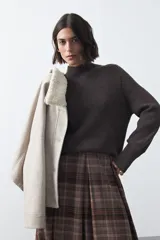 Polera de tejido de punto color blanco, con cuello alto y mangas largas con puños ajustados. Presenta un diseño minimalista de silueta relajada.