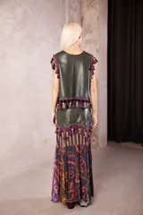 Falda larga de cuero verde oliva con diseño de paneles. Presenta una sección superior de cuero con un galón decorativo de borlas en tonos morados y verdes, y una sección inferior de tela fluida con estampado floral en tonos violeta, morado y verde.