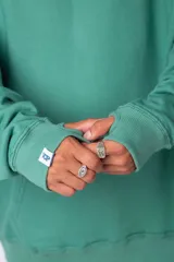Buzo canguro oversize de algodón rústico, color gris claro, con capucha y cordones ajustables con logo estampado. Presenta un diseño gráfico pequeño en el pecho y detalles estampados en la manga.
